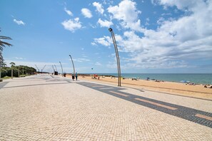 Une promenade dallée qui mène à une plage où l’on trouve des parasols et des gens.