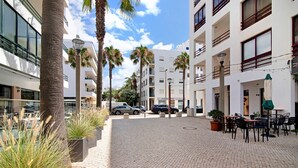 Ein gepflasterter Innenhof mit Palmen, Außenbestuhlung und modernen Gebäuden im Hintergrund.