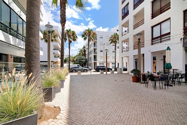 A paved courtyard with palm trees, outdoor seating, and modern buildings in the background.