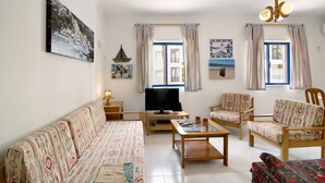 Ein Wohnzimmer mit einer Couch, Sesseln, einem Couchtisch, einem Fernseher und einem Bücherregal.