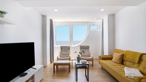En moderne stue med et fladskærms-tv, to lænestole, en sofa, et sofabord og en potteplante.