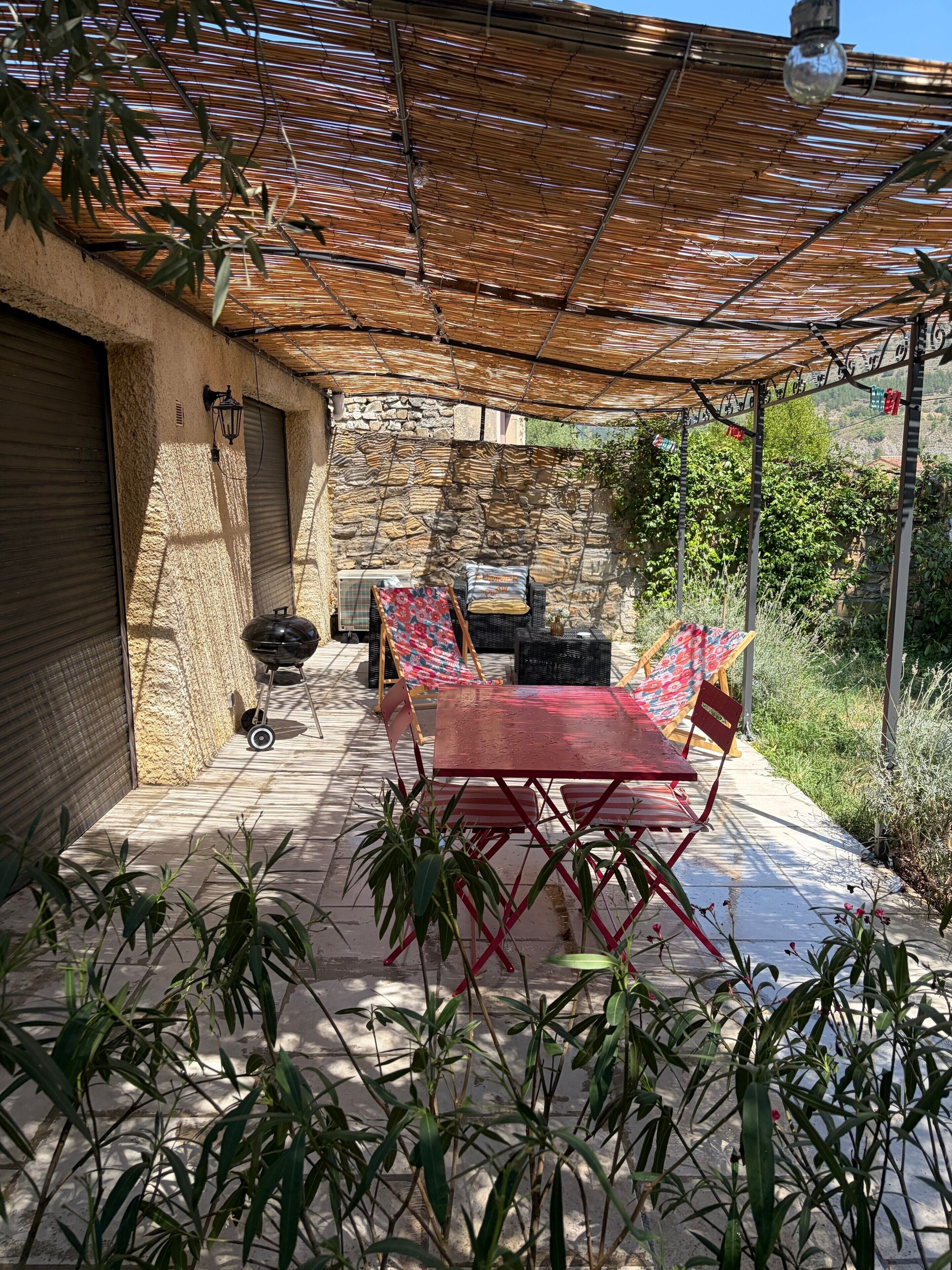 An outdoor patio with a table and chairs, a grill, and a stone wall.