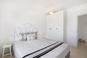 Une chambre à coucher comprenant un lit, une table de chevet, une lampe, une armoire et un luminaire suspendu.