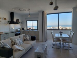 Una sala de estar moderna con sofá, mesa de comedor, sillas y vista al mar.