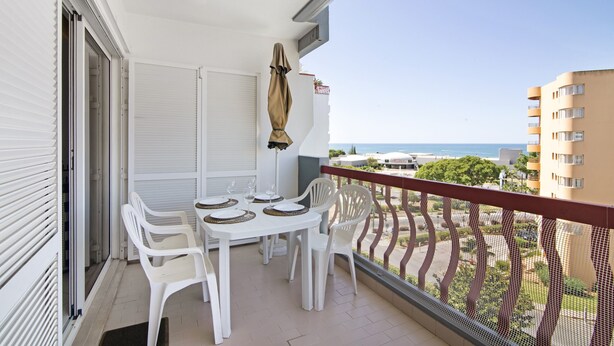Een balkon met een tafel gedekt voor twee personen, witte plastic stoelen, en een overdekt terras.