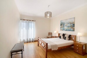 Ein Schlafzimmer mit einem hölzernen Bett, Nachttischen, einer Bank, einem Fenster mit Vorhängen und einem Gemälde an der Wand.