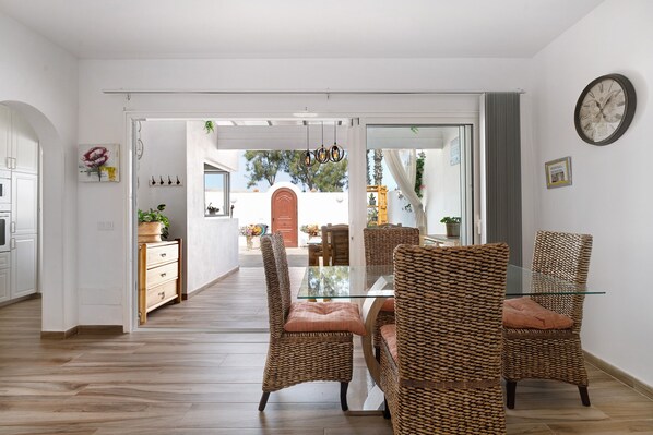 Comedor con sillas de mimbre, una mesa de vidrio y vista a un patio exterior.