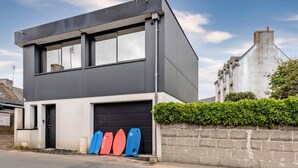 Un edificio moderno a due piani con un basculante, una porta nera e una fila di tavole da surf all'esterno.