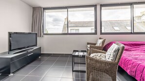 Una stanza moderna con una TV a schermo piatto, un letto con copriletto rosa, una sedia in vimini e un tavolino.