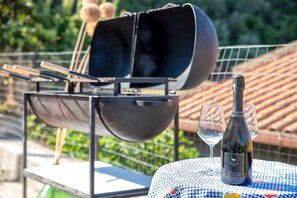 A grill with skewers, a bottle of wine, and glasses on a table.