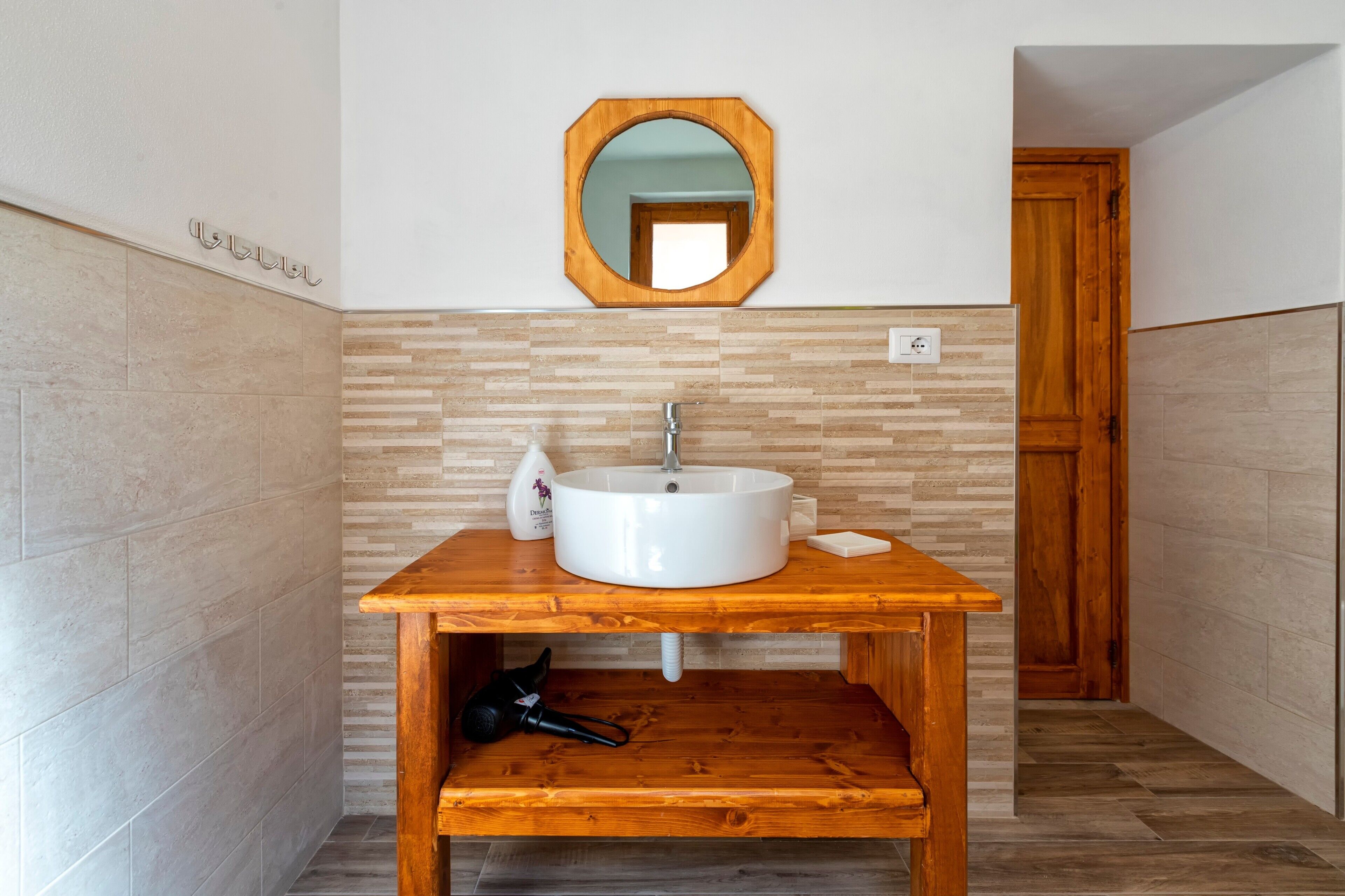Une salle de bain avec un meuble-lavabo en bois, un lavabo blanc, un miroir et un sèche-cheveux.