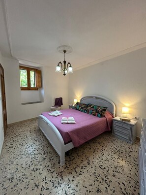 Una camera da letto con un letto, un comodino, una lampada, una finestra e un lampadario.