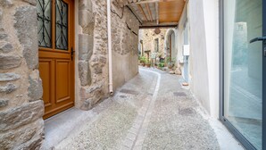 Un bâtiment en pierre avec une porte en bois, un étroit passage et une porte vitrée donnant sur un patio.