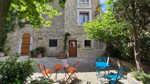 Un bâtiment en pierre doté d’une cour, d’un espace extérieur aménagé pour s’asseoir et d’un arbre.