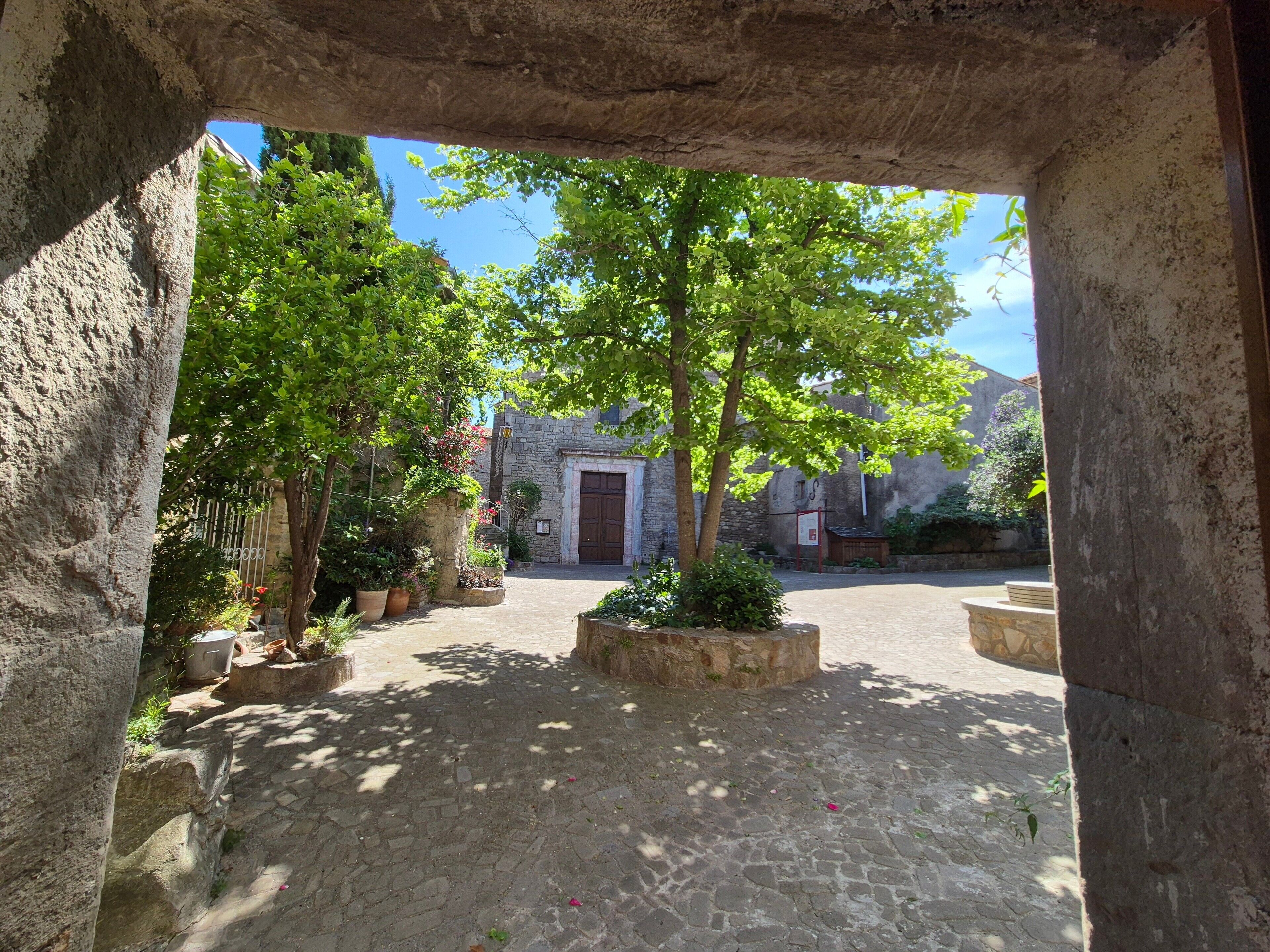 An outdoor courtyard with stone walls, potted plants, and a central door.