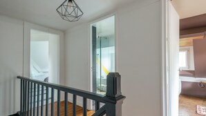 Un escalier avec une rampe noire menant à une pièce dotée d’une porte blanche et d’une douche en verre.