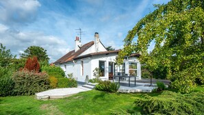 Une maison blanche avec un porche abrité, une pelouse et de la verdure tout autour.