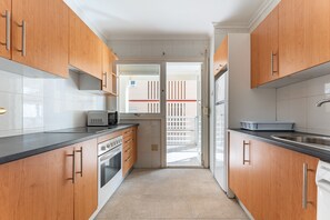 A narrow kitchen with wooden cabinets, a microwave, and a refrigerator.