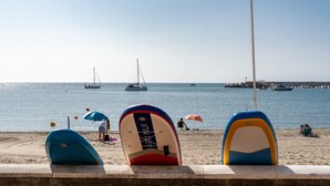 Ein Strand mit gestapelten Surfbrettern, einem klaren Himmel und Booten im Wasser.