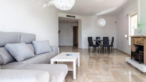 Ein modernes Wohnzimmer mit einer grauen Couch, einem weißen Couchtisch, einem Kamin und einem Essbereich mit Stühlen.