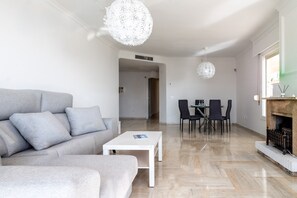 A modern living room with a grey sofa, a white coffee table, a fireplace, and a dining area with chairs.