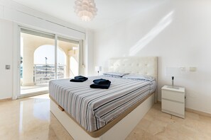 A bedroom with a large bed, a bedside table, a nightstand, and a view through a glass door.