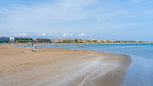 Une plage avec un rivage sablonneux, quelques personnes et des bâtiments en arrière-plan.