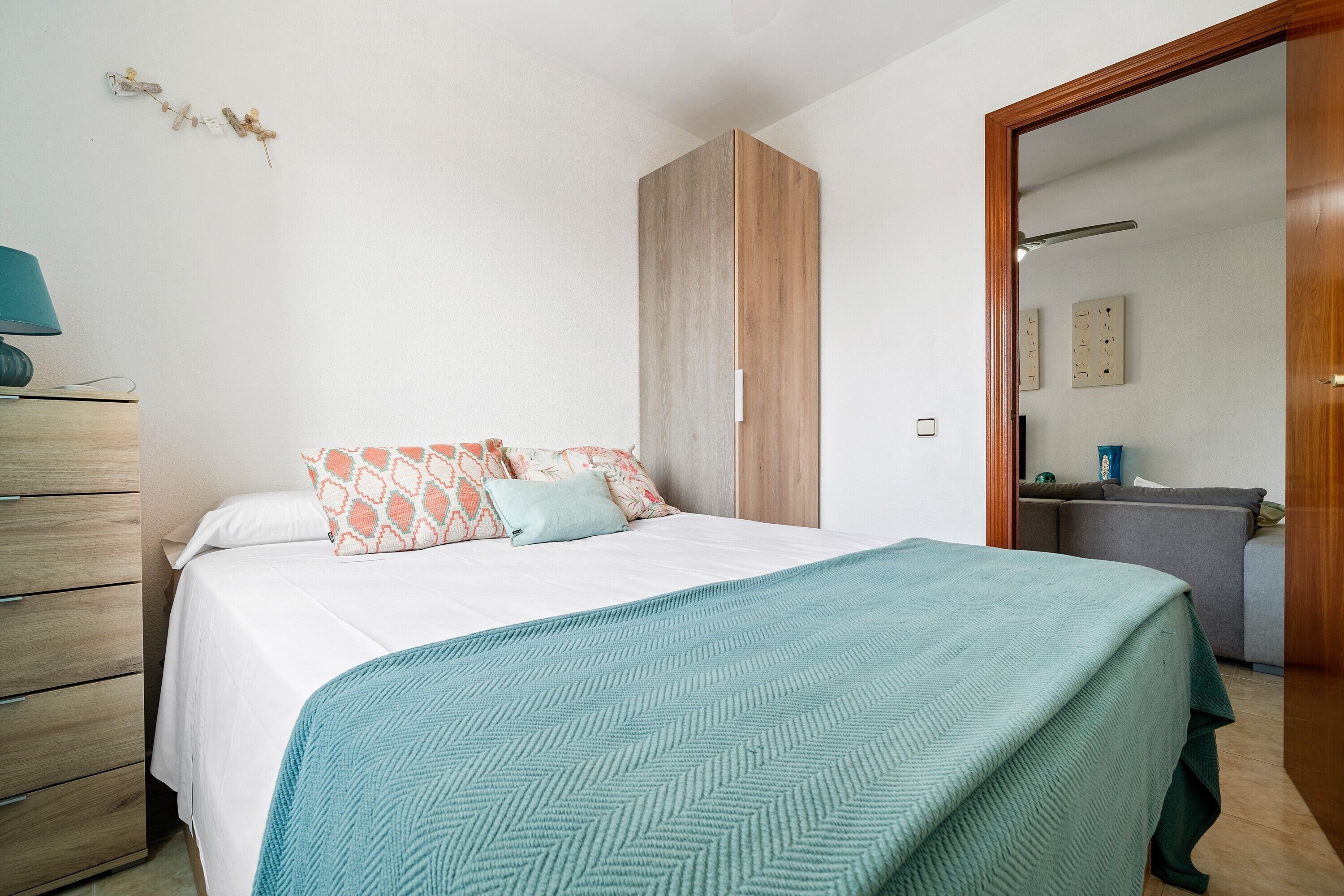 Ein Schlafzimmer mit Bett, Kommode, Kleiderschrank und einem durchgehenden Türrahmen sichtbarem Badezimmer.