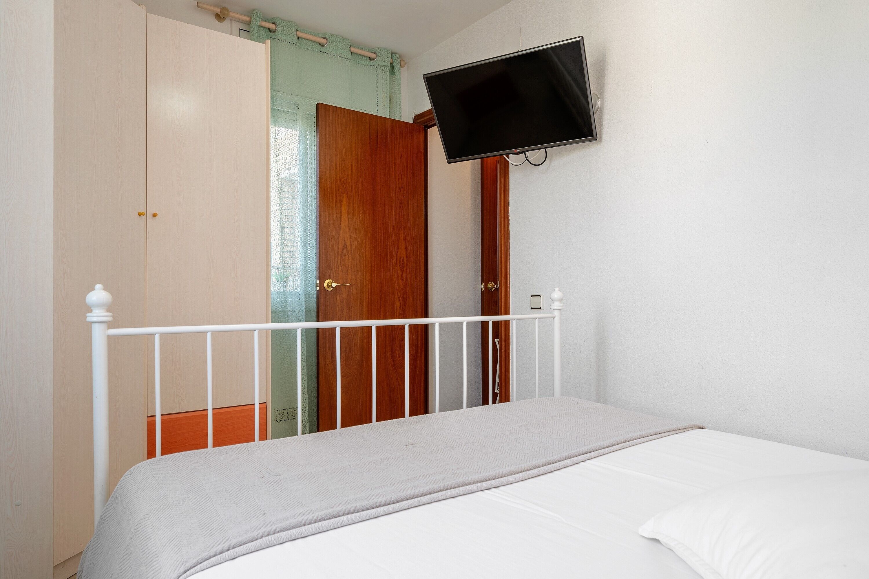 Une chambre à coucher avec un lit, un téléviseur fixé au mur et une armoire.