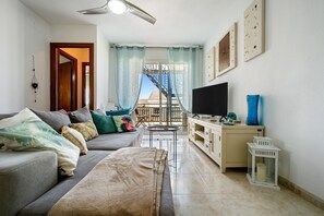 A living room with a sofa, TV, and a view of a building outside. - Apartment 'Atico Pepe Y Rosi' with Sea View, Wi-Fi and Air Conditioning (Cunit)