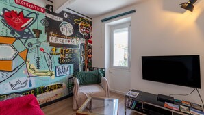 Un salon avec une fresque murale, un canapé, une table basse en verre, un téléviseur et une bibliothèque.
