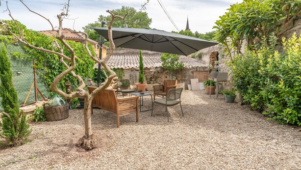 Un espace patio aménagé avec une table et des chaises, un grand parasol et des plantes en pot.