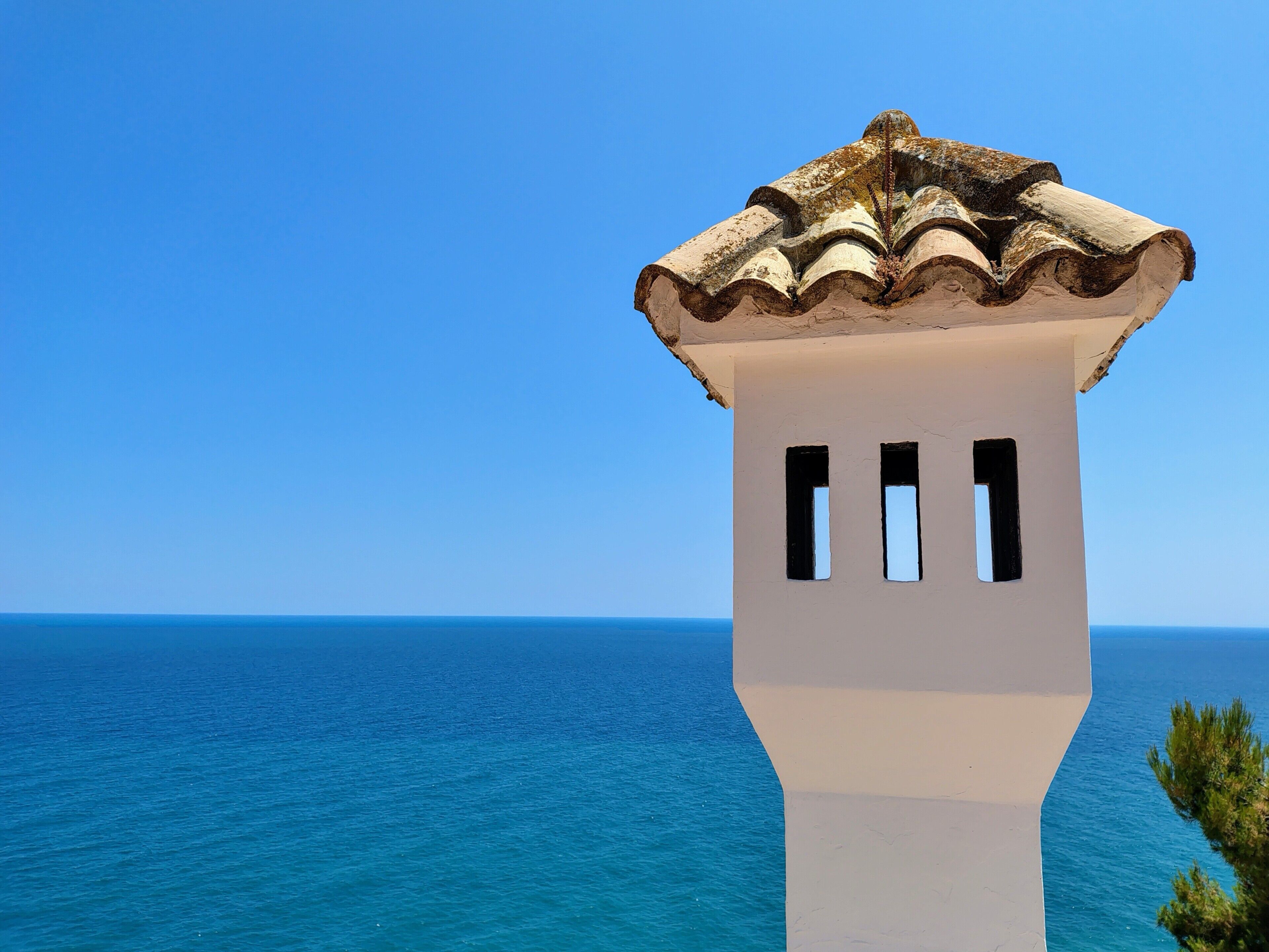 Un bâtiment situé sur la côte, avec une façade blanche et un toit recouvert de tuiles, qui offre une vue sur la mer.