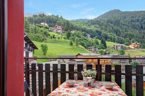 A balcony with a table, a railing, and a view of a village with houses and mountains.