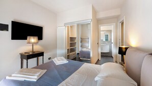 Ein Hotelzimmer mit Bett, Nachttischen, Fernseher, Kleiderschrank und einem durchgegangene Tür sichtbaren Badezimmer.