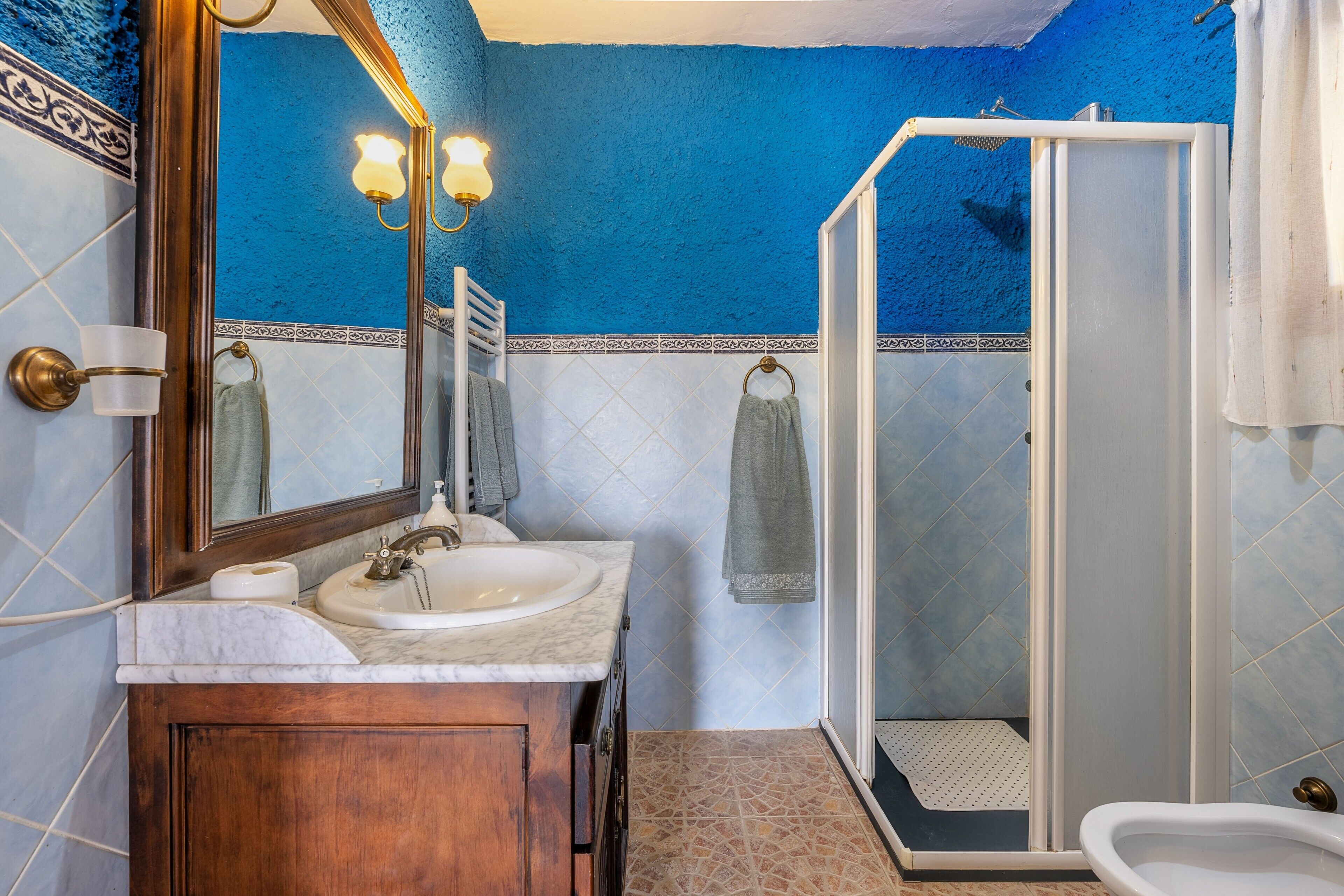 A bathroom with a marble sink, a mirror, a shower, and a tiled floor.
