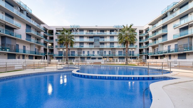 Et hotel med flere etager, en central swimmingpool, altaner og palmer.