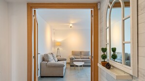 En gang der fører til en opholdsstue med to sofaer, et lille bord, en lampe og et vindue med udsigt.
