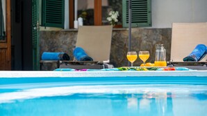 Un área junto a la piscina con sillas de descanso, una mesa con bebidas y un muro de piedra al fondo.