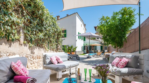 Un patio con mobiliario exterior, una mesa con bebidas y vistas a un edificio con piscina.