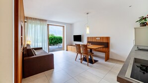 A modern hotel room with a sofa, dining table, chairs, a TV, and a kitchen area. - Apartment "Langstein Golden" with Mountain Views, Shared Terrace and Wi-Fi (Coldrano)
