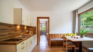 Een moderne keuken met houten kastjes, een eethoek met een bank en uitzicht op groen.