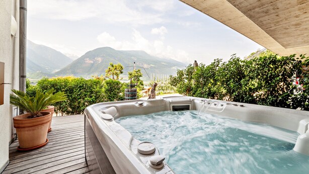 Een hottub met uitzicht op de bergen, een houten terras en potplanten.