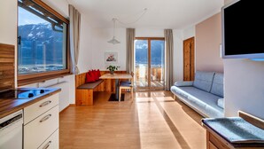 A modern kitchen with a stove, wooden cabinets, and a dining area with a bench and table. - Apartment "Langstein Rose" with Mountain View, Balcony and Wi-Fi (Coldrano)