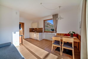 A modern kitchen with wooden cabinets, a dining area with a wooden table and chairs, and a view of a mountain through a window. - Apartment "Langstein Rose" with Mountain View, Balcony and Wi-Fi (Coldrano)
