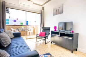 En moderne stue med sofa, lænestol, fjernsyn og en balkon med udsigt.