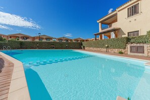Una piscina con cubierta de madera, rodeada de edificios con balcones y un cielo azul despejado.