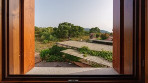 Vista a través de una puerta de madera abierta, mostrando un edificio con varios tejados y un paisaje verde exuberante.