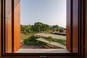 A view through an open wooden door, revealing a building with multiple roofs and a lush green landscape.