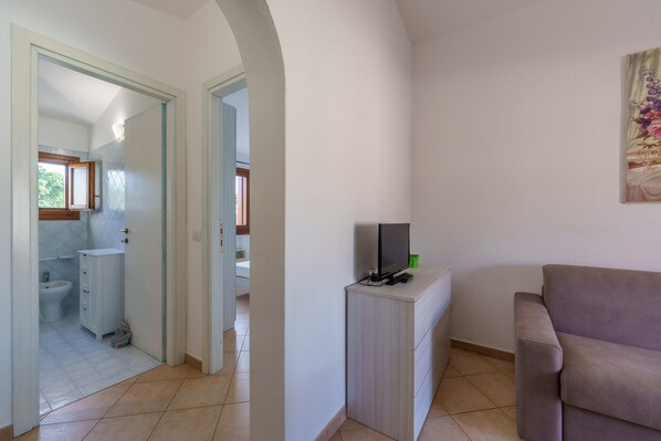 Una habitación con sofá, televisión sobre un mueble bajo, armario y baño a la vista a través de una puerta abierta.